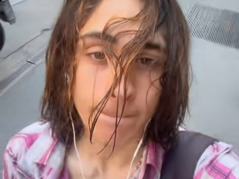 trenchmafia con i capelli bagnati sul viso, camicia a quadri rosa e auricolari alle orecchie