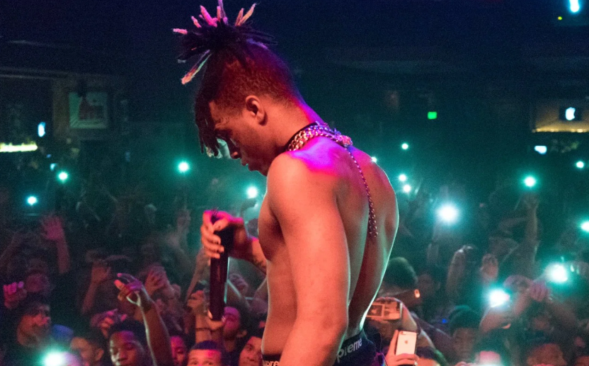 XXXTENTACION a torso nudo sul palco con la testa china, davanti a un pubblico che illumina la sala con i telefoni