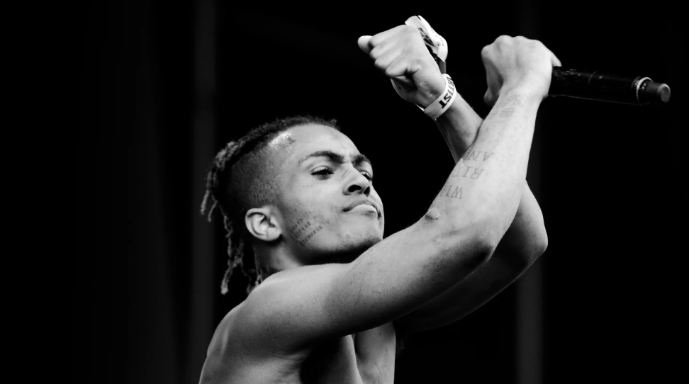 Riot di XXXTENTACION: il rapper sul palco in bianco e nero, con le braccia alzate e il microfono in mano