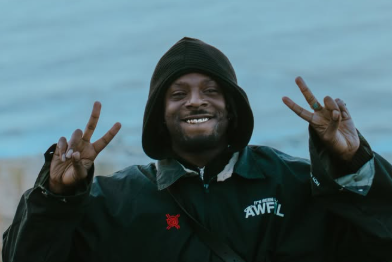 Foto di Isaiah Rashad, autore di It's Been Awful. Indossa un poncho verde e sorride guardando in telecamera.