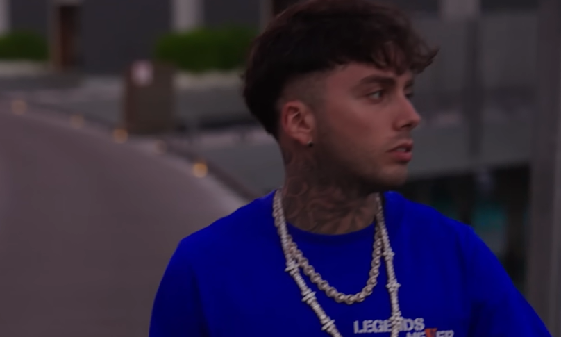 Tony Boy di profilo con maglia blu e catene, in una scena di un video
